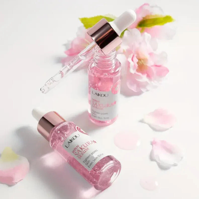 Suero facial coreano de sakura LAIKOU en envase rosa con gotero, flores y pétalos.