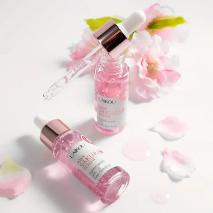 Suero facial coreano de sakura LAIKOU en envase rosa con gotero, flores y pétalos.