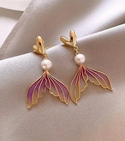 Pendientes dorados con perla y colgante de ala de mariposa en tonos rosa y lila sobre tela gris