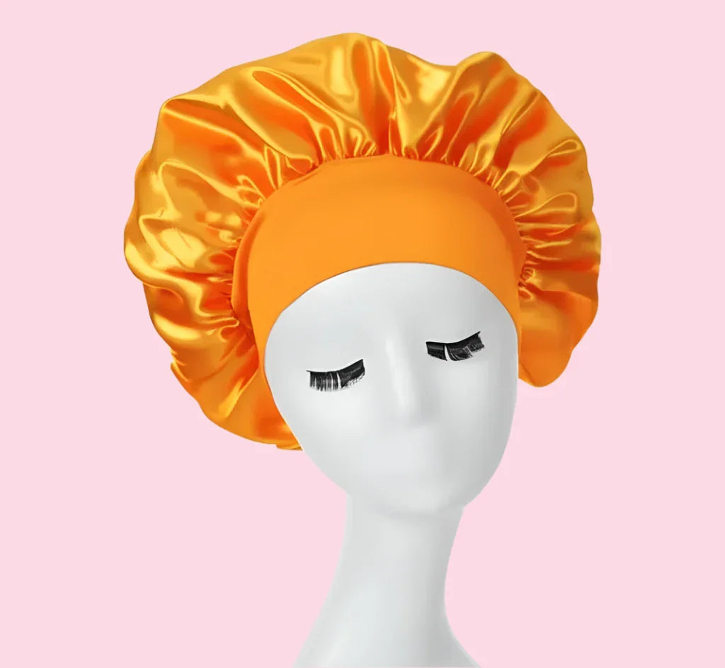 Gorro de satén naranja para cabello, accesorio de belleza, fondo rosa.
