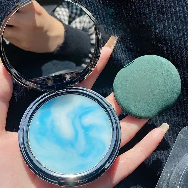 Polvo compacto de maquillaje coreano con tapa verde y textura azul marmoleada en mano